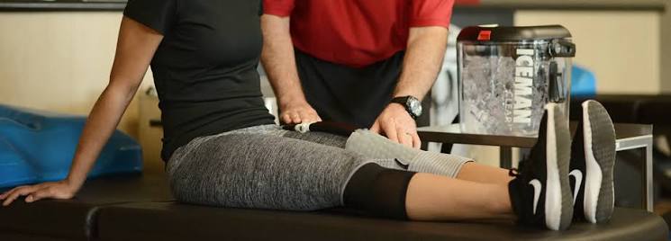 Physiotherapist fitting an ICEMAN Clear3 knee wrap with the ICEMAN cold therapy unit beside the treatment table