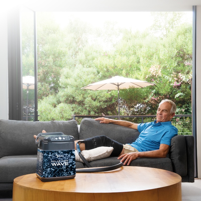 Patient relaxing at home with a Polar Care Wave cold therapy unit and knee wrap during recovery