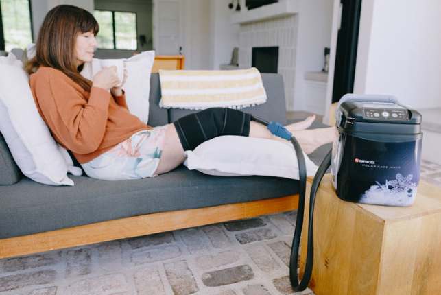 Woman resting on a couch at home with a Polar Care Wave leg wrap fitted