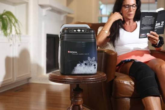 Woman reading at home while the Polar Care Wave runs beside her with a knee wrap